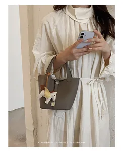 Minimalist leather bucket bag with cute winged horse charm and elegant padlock design.