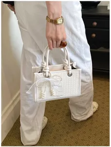 Gedetailleerd overzicht van de elegante witte geweven handtas met een mooie parelstrik.
