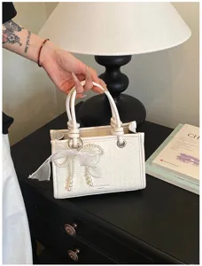 Gedetailleerd aanzicht van de witte geweven handtas met elegante parel strik charm.