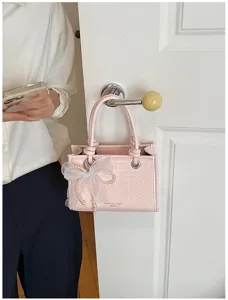 Roze geweven handtas detail met elegante witte mesh parel strik en metalen accenten.