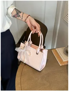 Detailopname van de elegante roze geweven handtas met parel strik en stijlvolle knoop handvatten.