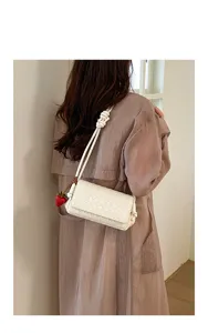 White woven shoulder bag for women, stylish underarm bag with cute strawberry charm accessory.