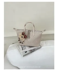 Detailed view of cream woven dumpling handbag featuring a cute teddy bear charm and metal zipper.