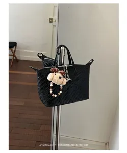Detailed view of the black woven dumpling bag with cute puppy plush charm and beaded chain.