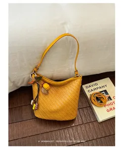 Detailed view of yellow woven shoulder bucket bag with decorative charm and textured surface.
