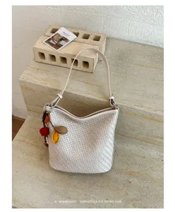 Detailed view of a simple retro woven bucket shoulder bag in off-white with delicate texture.