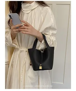 Detailed view of women minimalist black bucket handbag with metal lock and leather texture.