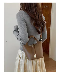 Brown leather bucket bag detail view, classic lock charm design, elegant retro handbag.