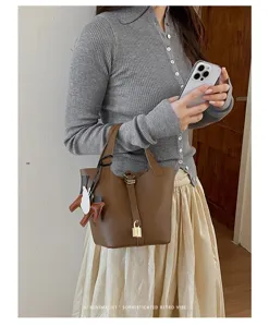 Stylish minimalist brown leather bucket handbag featuring elegant horse charm and lock detail.