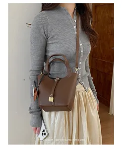 Brown leather bucket bag with metal lock detail worn by model in minimalist style setting.