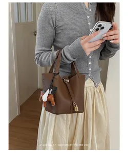Stylish brown leather bucket bag for women, chic minimalist handbag with lock and charm.