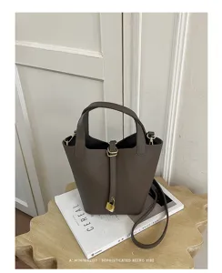 Close-up detail of the dark grey leather bucket bag with gold lock and handle on a minimalist table.