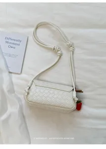White woven leather crossbody bag detail, featuring unique knotted strap and cute strawberry charm.