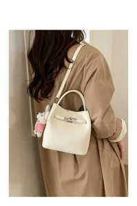 Detailed view of women's white litchi pattern bucket bag with chic lock closure and cute bear charm.