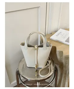 Detail view of cream bucket bag with metal lock clasp and handle, minimalist style scene.