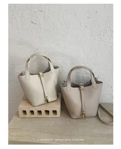 Detail shot of minimalist leather bucket bags in cream and taupe with chic metal locks.