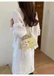 Detailed view of quilted chain shoulder bag in soft yellow with cute bear pendant and bow.