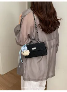 Detail view of black quilted crossbody bag with chain strap and cute bear charm pendant.