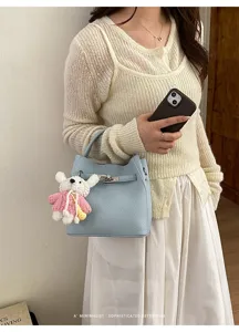 Close-up detail of the light blue litchi pattern bucket bag with cute knit bear charm.
