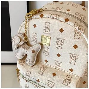 Primo piano dettaglio dello zaino beige con stampa orsacchiotto e placca logo in metallo.