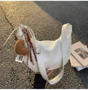 Detailed view of white vintage hobo shoulder bag with cute heart charm and outdoor street style.