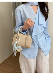 Vue détaillée d'un élégant sac Boston beige avec charmant pendentif ours et tenue chic.
