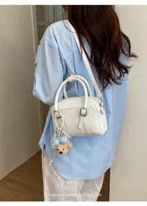 Sac Boston en cuir grainé blanc en détail avec pendentif ours élégant et bandoulière chic.