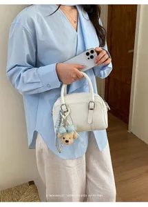Gros plan élégant d'un sac à main Boston blanc avec charmant pendentif ours au style rétro.