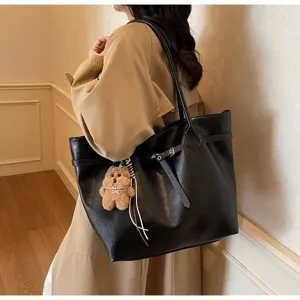 Black leather shoulder tote bag for women with chic buckle and plush bear pendant details.