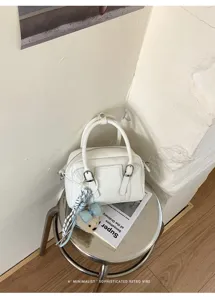 Gros plan détaillé du sac Boston blanc avec boucles en métal et charmant pendentif d'ours.