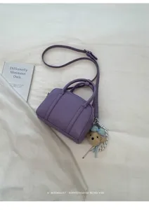 Détails du mini sac Boston violet avec poignées supérieures et pendentif en peluche d'ours.