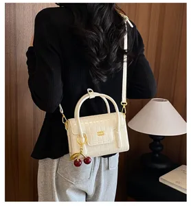 Detail view of a stylish white crocodile embossed mini handbag with cute cherry charm.