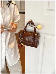 Brown crocodile pattern handbag detail, stylish crossbody bag with cherry charm and metal clasp.