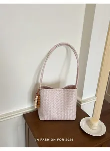 Gros-plan d'un sac seau en cuir tressé rose avec bandoulière et charm de perles sur table.