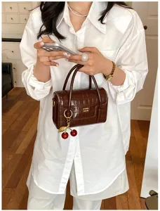 Detailed view of women's brown crocodile pattern handbag with stylish cherry charm and top handle.