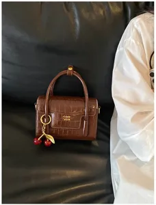 Detail view of the brown crocodile pattern mini handbag with a cute cherry metal charm pendant.