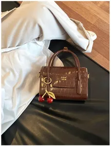 Brown crocodile pattern handbag with cherry charm, stylish top-handle crossbody bag for women.