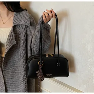 Close-up of black bowling shoulder bag with double straps, metal hardware, and chic charm detail.