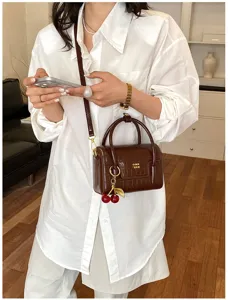 Detailed view of the brown crocodile pattern handbag with charming cherry pendant and hardware.