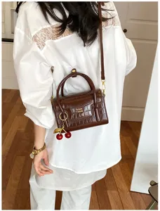 Chic brown crocodile pattern small crossbody bag with cute cherry charm for women daily use.