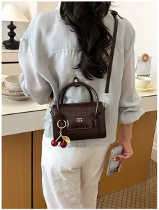 Detailed close-up view of the dark brown crocodile pattern handbag with cute cherry charm.