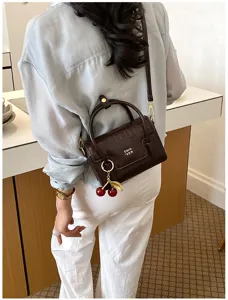 Detail shot of a stylish brown crocodile pattern crossbody bag with a chic cherry charm.