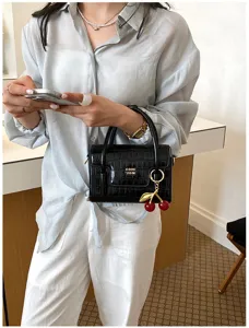 Fashionable black crocodile pattern handbag with cherry charm, chic top handle crossbody bag.