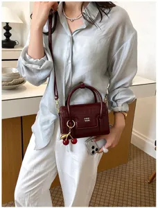 Women's chic burgundy crocodile pattern crossbody bag with cute cherry charm for autumn.