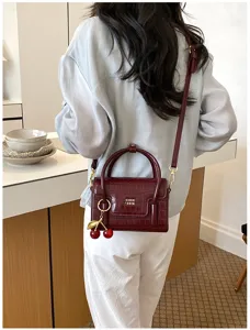 Detailed view of the burgundy crocodile pattern crossbody bag with cherry charm and gold hardware.