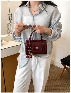 Close-up of burgundy croc-embossed top handle mini bag with cherry charm and gold text.