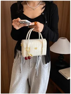 Detailed view of fashionable white crocodile pattern handbag with charming cherry pendant.
