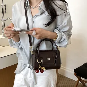 Stylish brown crocodile pattern crossbody bag for women with cute cherry charm and handle.