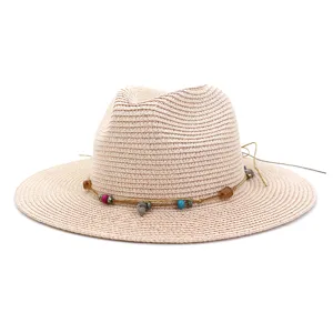 Detailopname van beige strooien fedora hoed met kleurrijke kralen en schelp touw decoratie.