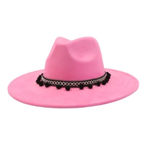 Pink suede fedora hat detail showcasing woven band and black pom-pom decorations closely.